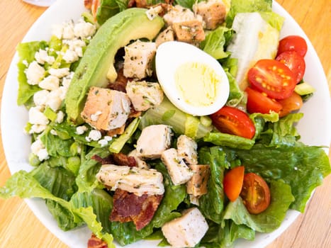 Grilled herb chicken, crisp bacon, boiled eggs, and cherry tomatoes on a bed of fresh lettuce with crumbled cheese