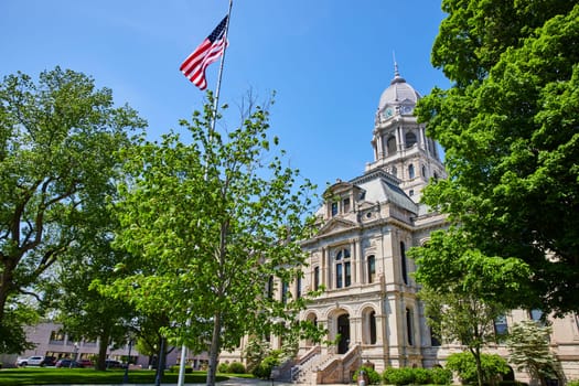 Majestic Kosciusko County Courthouse in Warsaw, Indiana, with a vibrant blue sky and American flag.