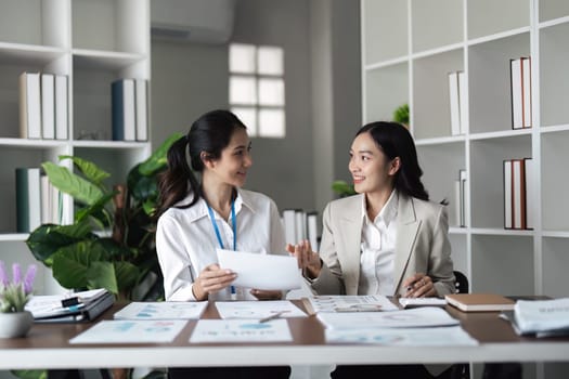 Two young businesswomen discussing reports and smiling at the office.