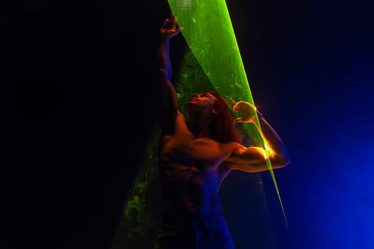 Sporty handsome man with long hair, naked torso abs portrait under colorful illumination, laser light, neon smoke club. Projection illusion mapping. Futuristic model.