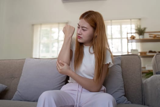 Young woman examining her arm indoors, feeling discomfort.