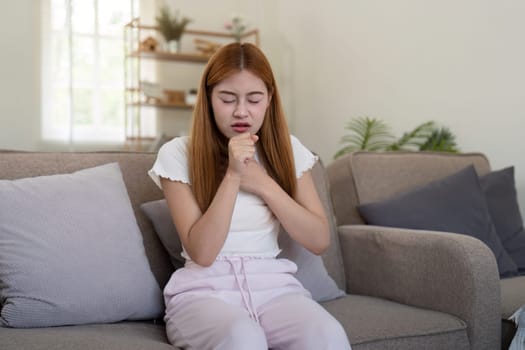 Young woman coughing while sitting on sofa at home.