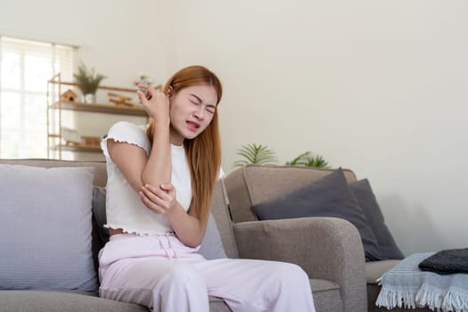 Young woman feeling pain in her elbow while sitting indoors.