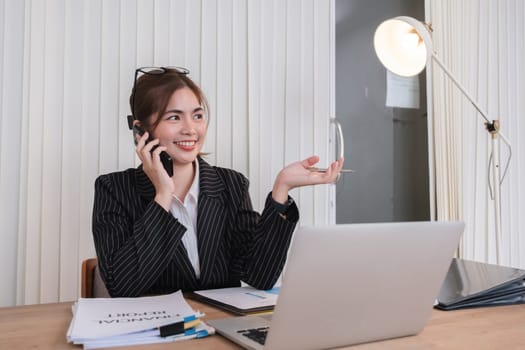 Beautiful accountant talking on the phone and calculating financial figures and calculating taxes for the company..