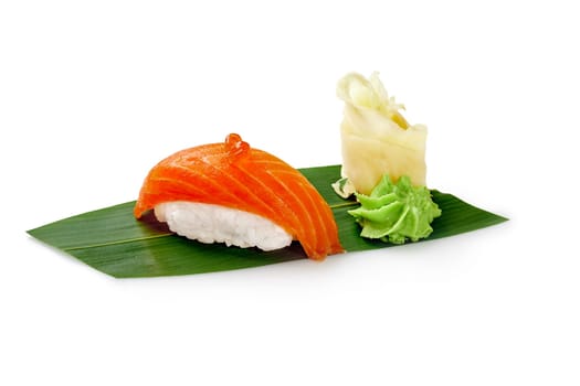 Delicious salmon nigiri sushi with roe, pickled ginger and wasabi served on green bamboo leaf isolated on white background. Traditional Japanese cuisine. Sushi bar menu concept