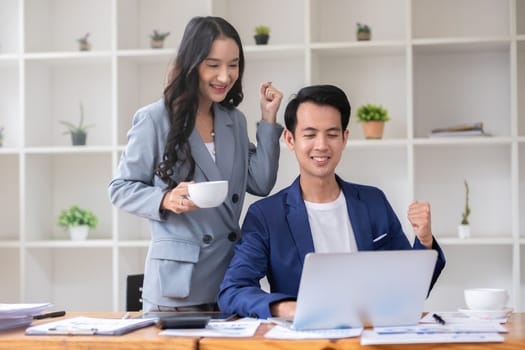 A young businessman and a successful Asian accountant happily celebrate together in the office..