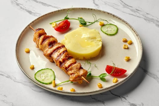 Grilled chicken fillet pieces on mini skewer served with creamy mashed potatoes, cherry tomato and cucumber slices garnished with green pea sprouts on marble surface. Delicious healthy dinner for kids