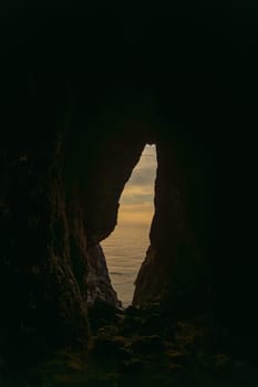 A cave with a small opening in the wall. The cave is dark and the sky is cloudy