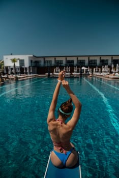 A lovely woman in a swimsuit sits by the pool, facing away from the pool. High quality photo