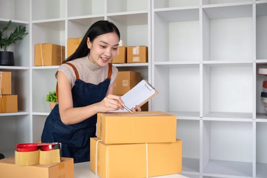 A small business owner receives product orders and writes shipping information on cardboard boxes in the home office to prepare for delivery..