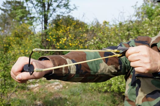 A man pulls the rubber band of a slingshot for a shot in the forest.