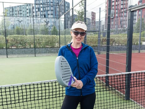 Portrait of positive young woman with racket and padel ball on tennis court. High quality photo