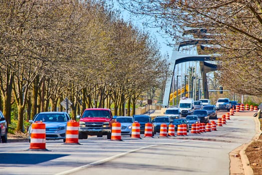 Dynamic urban scene with leafless trees lining a busy Fort Wayne street, showcasing traffic and roadwork under a clear sky.