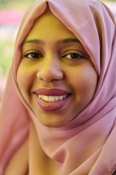 A Middle Eastern girl wearing a hijab, with a bright smile and a pink headscarf, captured in a close-up portrait exuding joy and positivity.