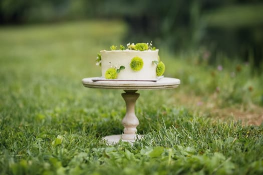 A beautifully decorated cake placed on a wooden stand, sitting gracefully in the middle of a green grass field.