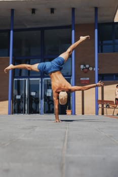 A man skillfully performs a handstand in front of a tall, modern building, showcasing strength and balance in an urban setting.