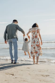 A family, accompanied by their child, walks peacefully along the sandy beach, enjoying the soothing rhythm of the ocean waves.