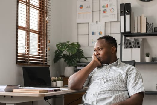 African American businessman feeling stressed while working using laptop Take notes on documents in the office and prepare work reports..