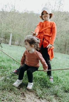 Portrait of two little beautiful Caucasian girls sisters having fun playing and fooling around with a rope on a spring day in a park in Belgium, close-up side view.