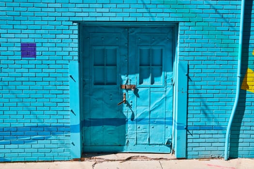 Aged turquoise doors with rust and graffiti in downtown Fort Wayne evoke urban decay and history.