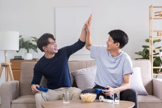 A fun lgbt male couple sits happily playing a pc game with a console joystick together..