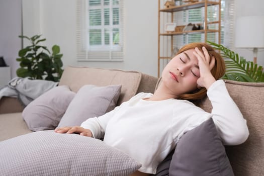 A young Asian woman in the living room was suffering from a headache due to accumulated stress due to health problems and lifestyle problems causing stress disorder..