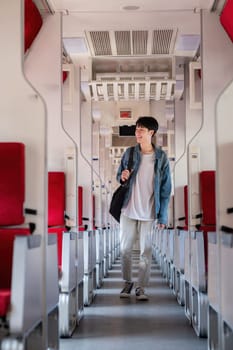 A young man holding a suitcase waits for a train at the train station for traveling..