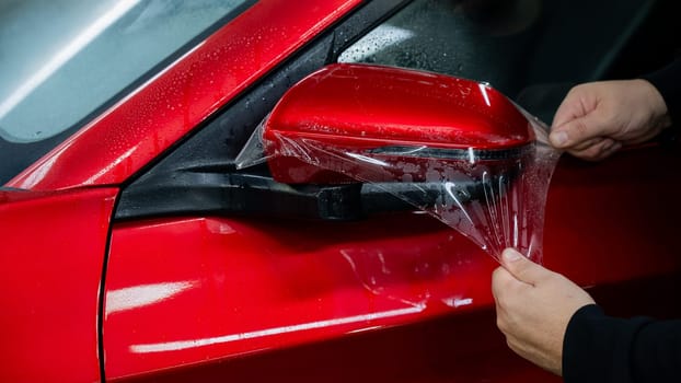 The master applies vinyl film to the side view mirror of a car