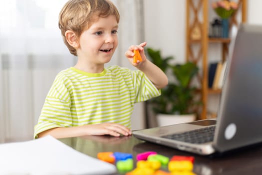 A young boy in a striped shirt smiles while interacting with educational toys during an online learning session at home