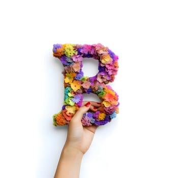 An isolated hand holding a rainbow letter "B" on a white background, representing the LGBTQIA community's inclusivity and diversity.