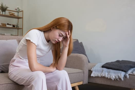 A young Asian woman in the living room was suffering from a headache due to accumulated stress due to health problems and lifestyle problems causing stress disorder..