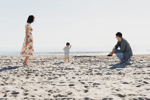 A family of three happily playing on the sandy beach with their small child, enjoying a sunny day by the ocean.