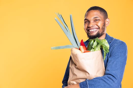 African american satisfied person purchasing organic lettuce and veggies from grocery store, supporting zero waste bio nutrition. Happy man eating fresh local products, delicious groceries.