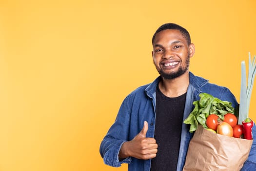 Charismatic friendly guy shows like gesture in studio, giving a thumbs up for fresh homegrown produce. Cheerful man recommending local farmers market for healthy eating, agreement.