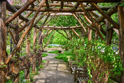 Serene garden pathway under a rustic pergola, lined with benches, at Warsaw Biblical Gardens, Indiana.