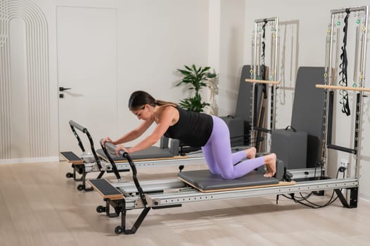 A pregnant woman does a plank on a reformer machine. Perinatal yoga