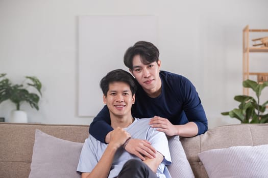 Happy Asian homosexual couple embrace on sofa in living room.