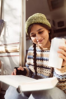 A fashionable, bohemian lady, rocking a hippie look, savors a hot drink on the house terrace. High quality photo