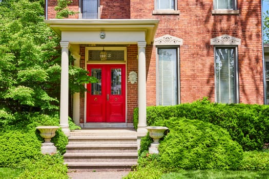 Charming red-brick house with vibrant door in Fort Wayne, surrounded by lush greenery and sunny skies.