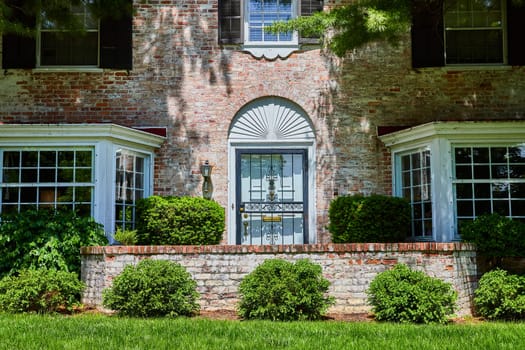 Traditional brick house with ornate ironwork door in Fort Wayne, Indiana, showcasing suburban elegance and lush landscaping.