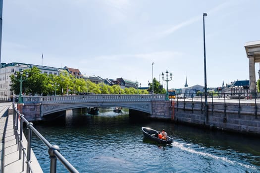 A boat with people is sailing along a water canal in the city. Copenhagen, Denmark - November 17, 2023