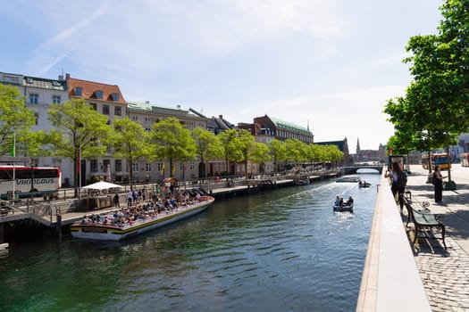 A boat with people is sailing along a water canal in the city. Copenhagen, Denmark - November 17, 2023