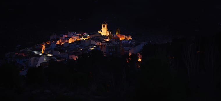 View from the hill of medieval historical village of Quesada in province of Jaen, with the illuminated bell tower and while houses in the night time. Beauty in Spain nature. Travel and tourism concept