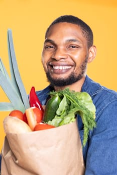 African american cheerful guy buying fresh bio greens and veggies from local farmers market, supporting zero waste healthy eating. Confident vegan man enjoying ethically sourced food.
