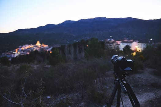 A digital camera placed on tripod, capturing the medieval village of Quesada in mountains Sierra de Cazorla at sunrise. Blurred mountains on the background. Travel photography. World photography Day