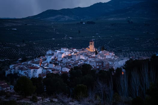 View from the hill of the medieval historical village of Quesada in the province of Jaen, at dawn with the illuminated bell tower and while houses. Beauty in nature. Travel and tourism concept. Spain