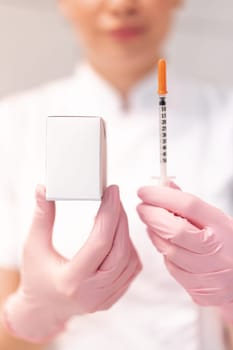 Cosmetologist in pink gloves showing skin lifting injection and mockup drug box. Crop blur dermatologist in white uniform demonstrating product mockup in clinic.