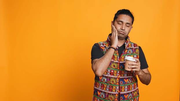 Sleepy man yawning and rubbing eyes. sipping coffee to wake up and gain energy. Exhausted person feeling fatigued after sleepless night, drinking caffeinated beverage, studio backdrop, camera B