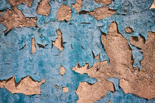 Aging blue paint peels to reveal textured beige layers in a stark portrayal of decay and transformation.