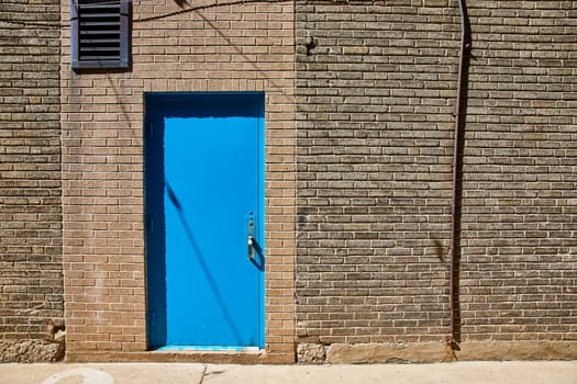 Bright blue door on a textured brick wall in downtown Fort Wayne, Indiana, under sunny skies.